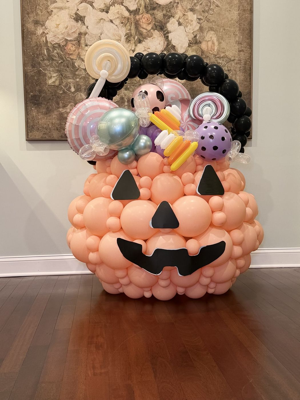 Giant jack-o'-lantern basket made of peach balloons with a black balloon handle and candy-swirl accents
